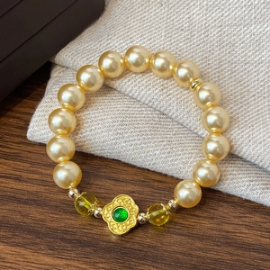 Bracelet de perles dorées avec pendentif fleur verte sur fond bois et tissu