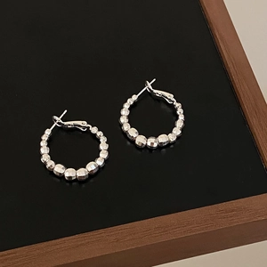 Macro shot of silver faceted crushed bead hoop earrings on a black jewelry stand