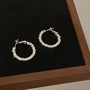Macro view of silver geometric circle earrings with textured cube segments and metal studs