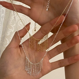 Detailed view of tassel fringe necklaces in gold and silver held by hand on fabric