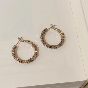 Vue macro de boucles d'oreilles créoles géométriques dorées au design industriel