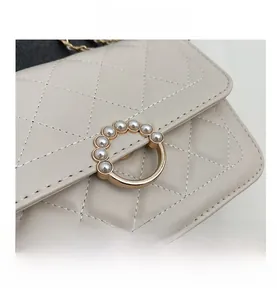 Detail of quilted beige crossbody bag featuring gold buckle with pearl embellishments
