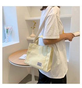Detail of cream canvas tote bag showing the reinforced handles and blue logo tag