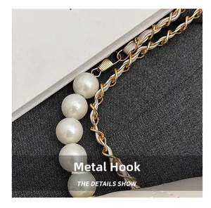 Close-up of pearl chain strap with gold hardware hook on a white quilted leather bag