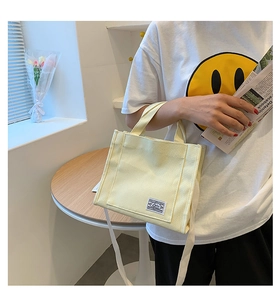 Detail of cream canvas mini tote bag featuring vintage label and long shoulder strap