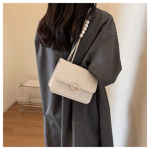 Detail of off-white quilted bag featuring pearl chain strap and gold pearl ring buckle