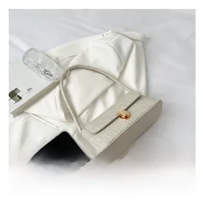 Détail d'un sac bandoulière crème motif crocodile avec fermoir doré à côté d'un téléphone