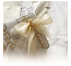 Dettaglio borsa trapuntata beige con elegante fiocco in seta sulla tracolla a catena