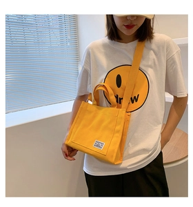 Detail showing the bright yellow canvas tote bag with shoulder strap and woven logo patch