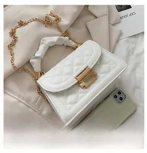 Close-up of white quilted crossbody bag with gold chain and cloud handle on beige blazer