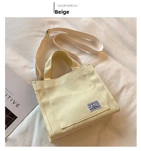 Detail view of a beige canvas tote bag featuring a vintage woven label and wide strap