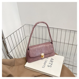 Détail du sac à main violet motif crocodile avec fermoir rotatif doré sur des livres