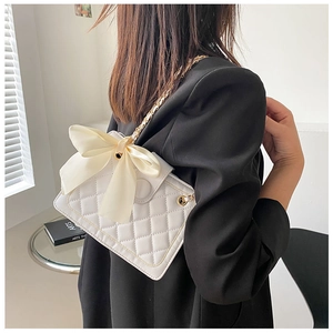 Dettaglio della borsa a catena in pelle trapuntata bianca con un grande fiocco di seta beige