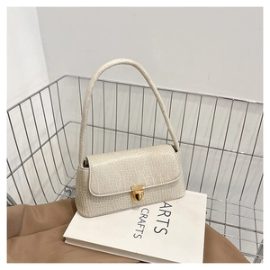 Détail du sac à bandoulière crème effet crocodile avec fermoir doré posé sur des livres