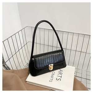 Détail d'un sac sous les bras en cuir croco noir avec boucle dorée sur des livres blancs