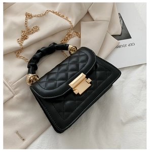 Detail of black quilted crossbody bag with golden buckle and ruched handle on beige fabric