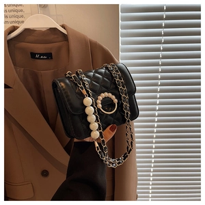 Close-up of black quilted shoulder bag with elegant pearl clasp and hanging pearl chain