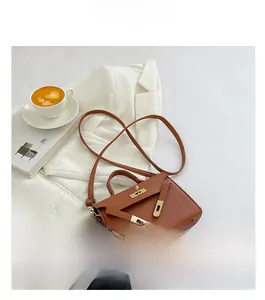 Brown mini Kelly style bag with lychee texture and gold hardware on white blazer background