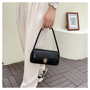 Détail d'un sac porté épaule noir à texture crocodile avec boucle cœur dorée pour femme