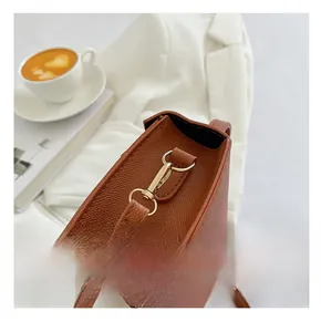 Detail of the brown textured leather handbag with gold metal clasp on a white blazer