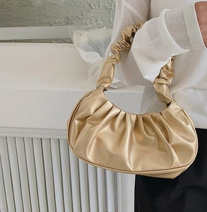 Detail of champagne gold ruched underarm bag with glossy pleated faux leather texture
