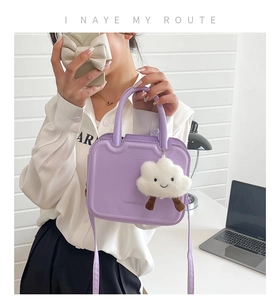 Close-up of light purple structured handbag with cute white plush cloud charm and strap