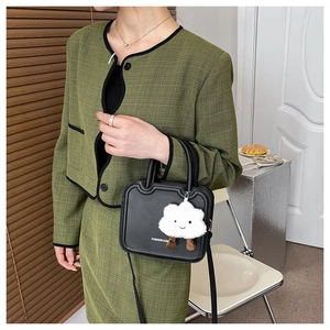 Detailed view of structured black leather handbag with a white cloud plush charm accessory