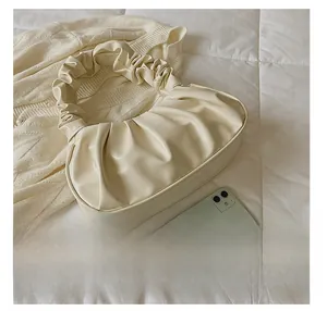 Detail presentation of a beige pleated cloud bag next to a smartphone for size comparison