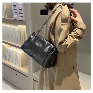 Detail view of the black pleated chain shoulder bag styled with a beige trench coat