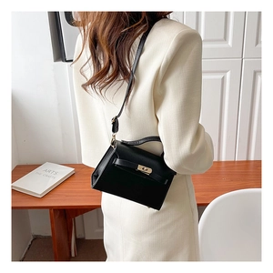 Detail shot of mini black trapezoid handbag with gold metal lock worn as crossbody bag