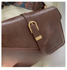 Detail of vintage brown leather handbag with gold horsebit buckle and colorful woven strap