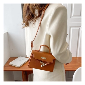 Caramel leather mini Kelly bag shown worn as a crossbody handbag in a modern office setting