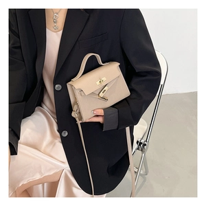 Detail of a beige mini leather handbag with a gold turn-lock worn with a black blazer