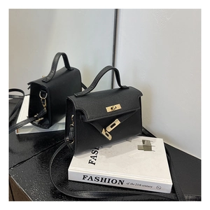 Close-up of black textured leather mini Kelly bag with gold metal clasp on books