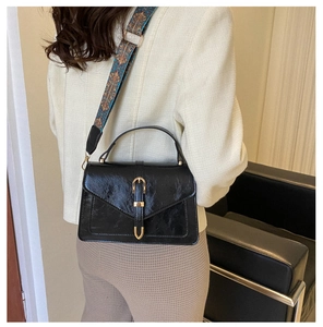 Detail of black vintage crossbody bag featuring gold buckle and embroidered strap