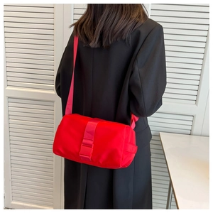 Macro detail of red nylon cylinder crossbody bag with buckle strap on black blazer