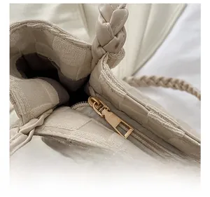 Close-up of golden zipper hardware and braided handle on cream woven tote bag
