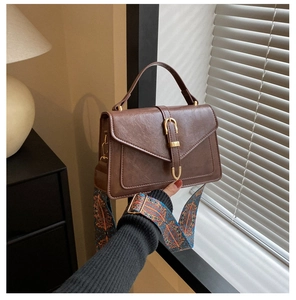 Detail of vintage brown PU leather bag with gold U-shaped buckle and patterned strap