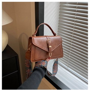 Detail of a brown leather crossbody bag with a vintage buckle and ethnic woven strap