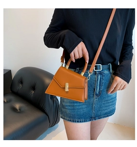 Brown leather trapezoid bag shown on shoulder in a lifestyle setting with sleek gold clasp