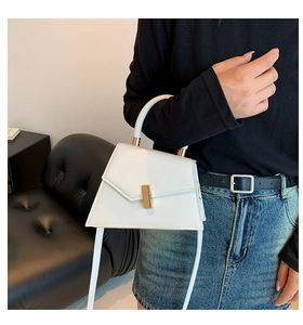 Dettaglio di una borsa a trapezio bianca con chiusura dorata indossata da una modella