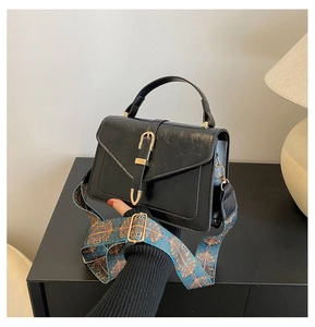 Detail of black leather flap bag with decorative gold buckle and wide ethnic pattern strap