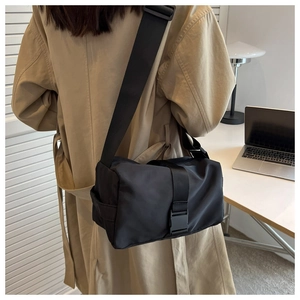 Detailed back view of a black nylon crossbody pillow bag worn over a beige trench coat