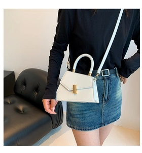 Detail of white trapezoid handbag showing gold twist lock and smooth leather texture