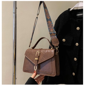 Detail of vintage coffee crossbody bag with patterned strap on a fashion coat backdrop