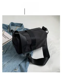 Close-up of a black nylon tote bag on a denim jacket showing the wide fabric strap