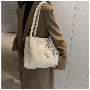 Detail of cream tote bag with checkered texture and woven handle on wool coat