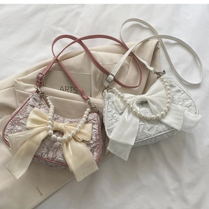 Dettaglio borsa in tessuto plissettato con fiocco grande e manico in perle eleganti
