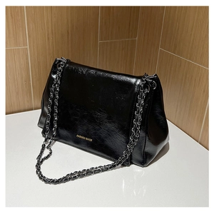Close-up of black wrinkled texture leather bag with metallic chain and gold lettering