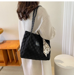 Detail of quilted black tote bag featuring woven straps and elegant silk scarf accessory